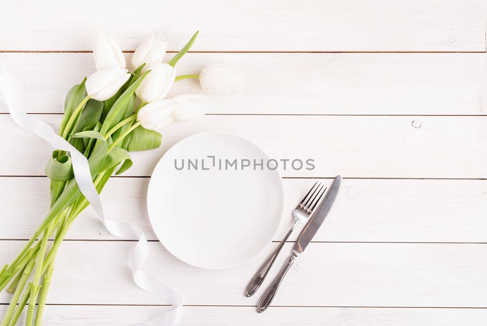 Concept Spring, Easter or Mother's Day. Festive table setting in white, white plate and tulips top view on wooden background