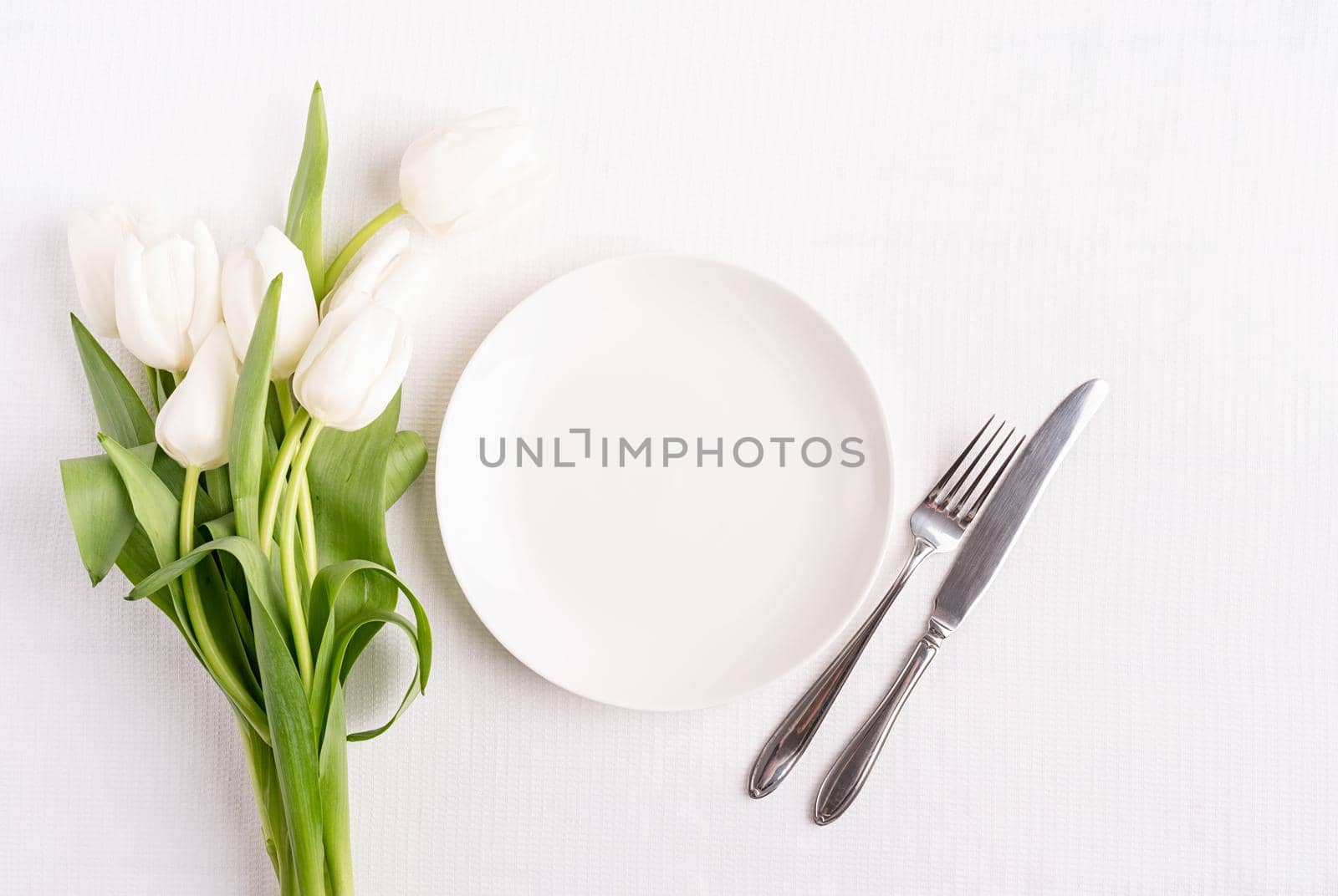 Concept Spring, Easter or Mother's Day. Festive table setting in white, white plate and tulips top view on background