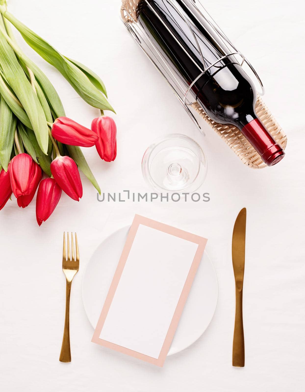 Mock up menu frame in restaurant or cafe. Top view of table setting with menu card, cutlery, fresh red tulips and wine on white fabric tablecloth