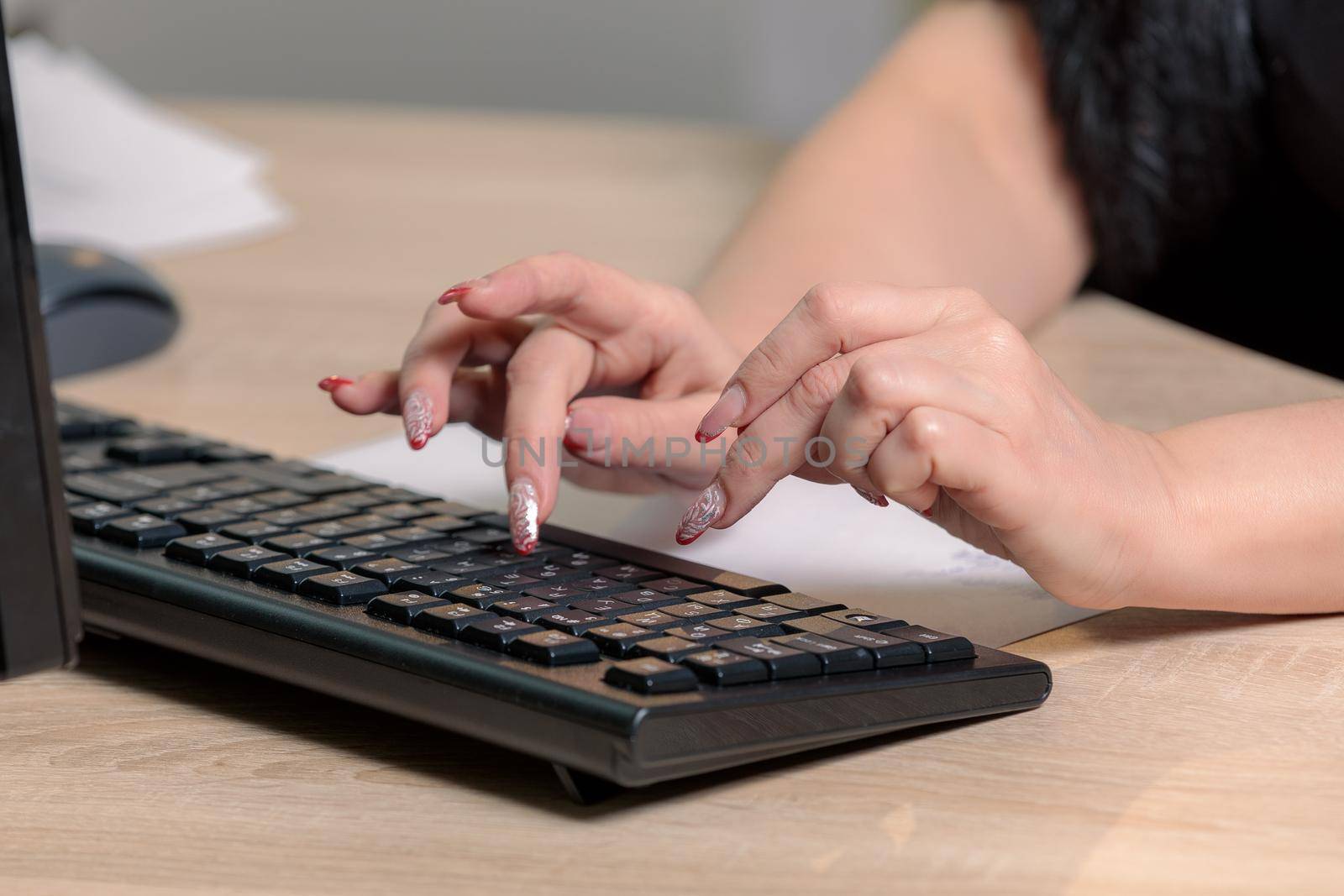 A woman director working in an office is sitting at a table, typing on a keyboard, checking documents. Close-up.