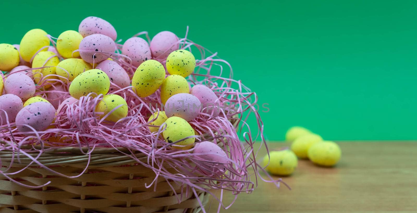 Colorful Yellow and Pink easter egg with freckle patterns on wooden table with copy space. Pink and Yellow easter egg inside a basket