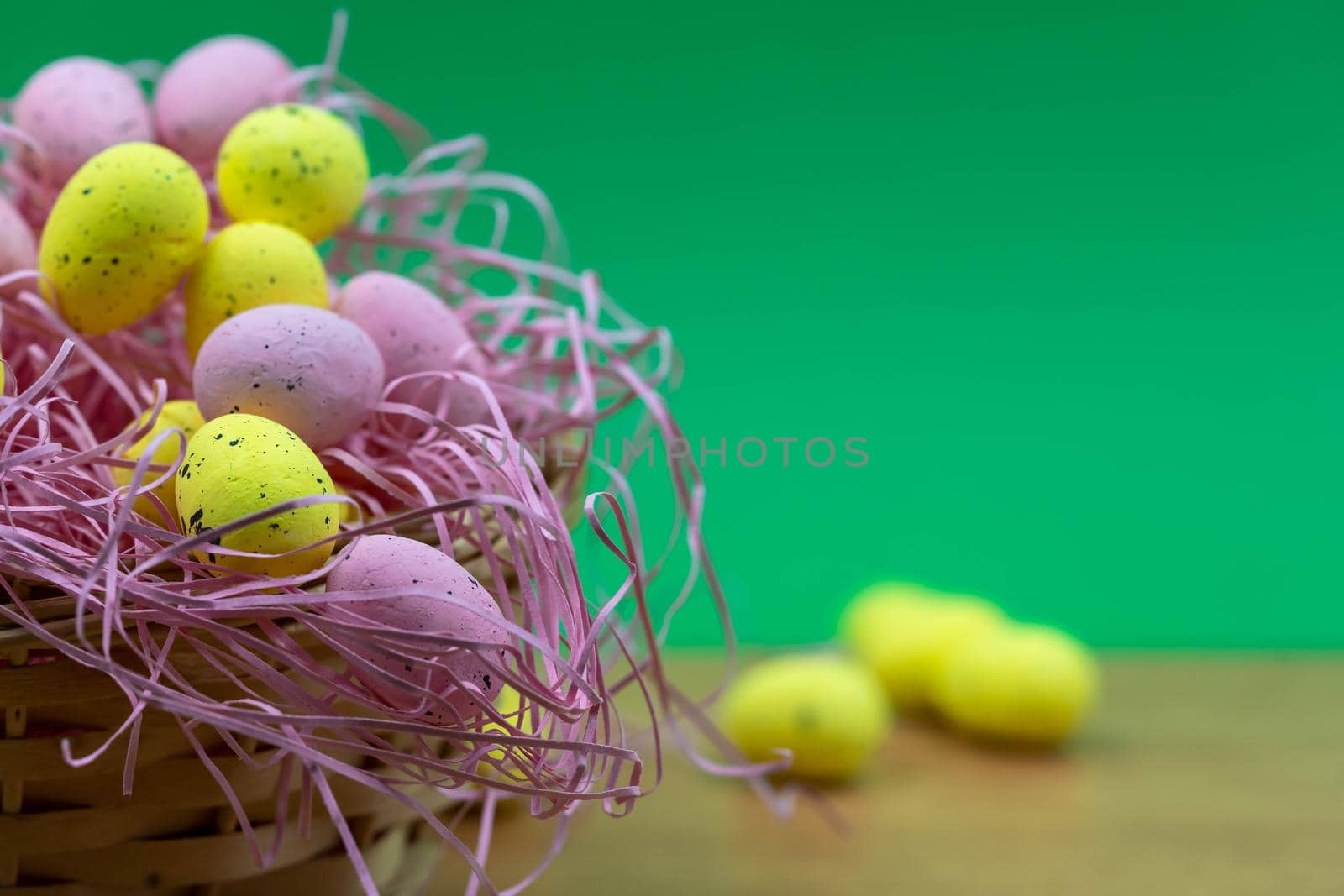 Colorful Yellow and Pink easter egg with freckle patterns on wooden table with copy space. Pink and Yellow easter egg inside a basket
