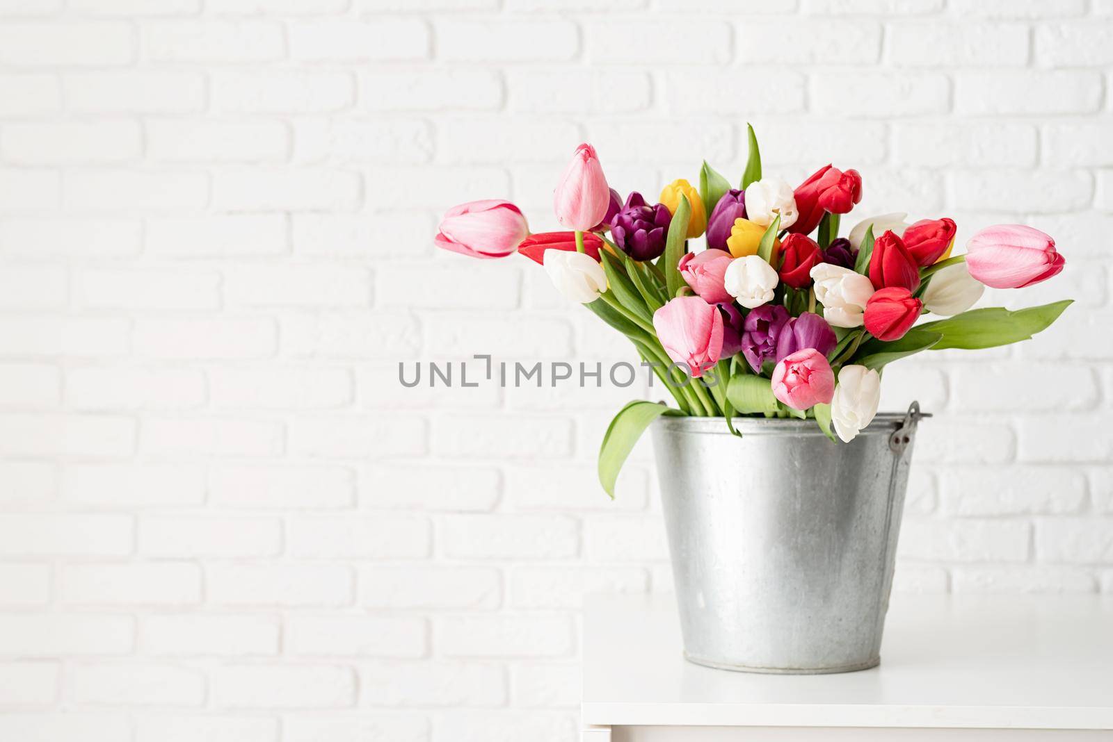 Bucket of tulip flowers over white brick wall background by Desperada