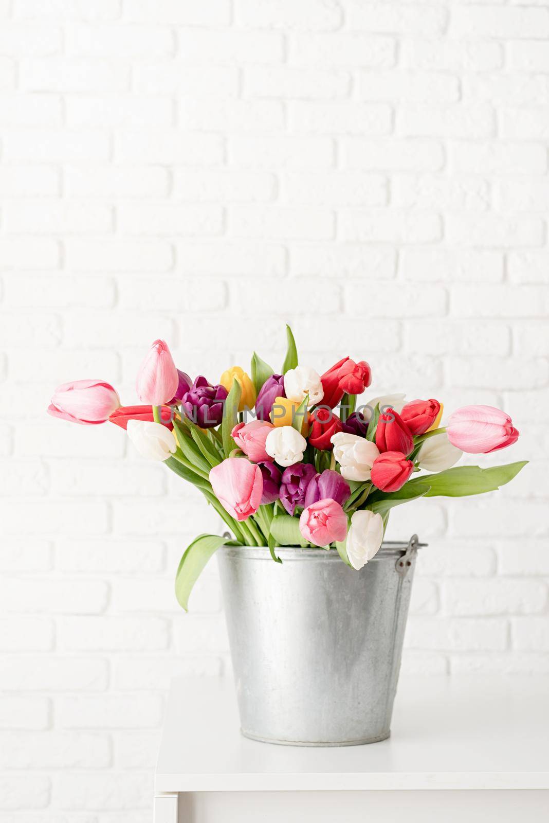 Bucket of tulip flowers over white brick wall background by Desperada