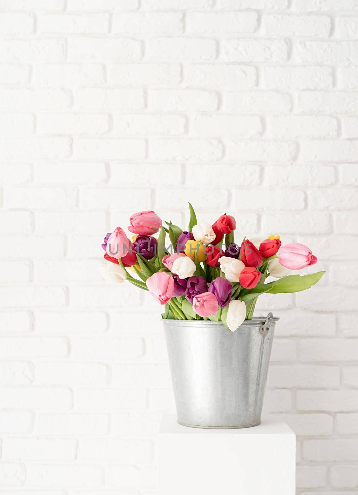 Bucket of tulip flowers over white brick wall background by Desperada