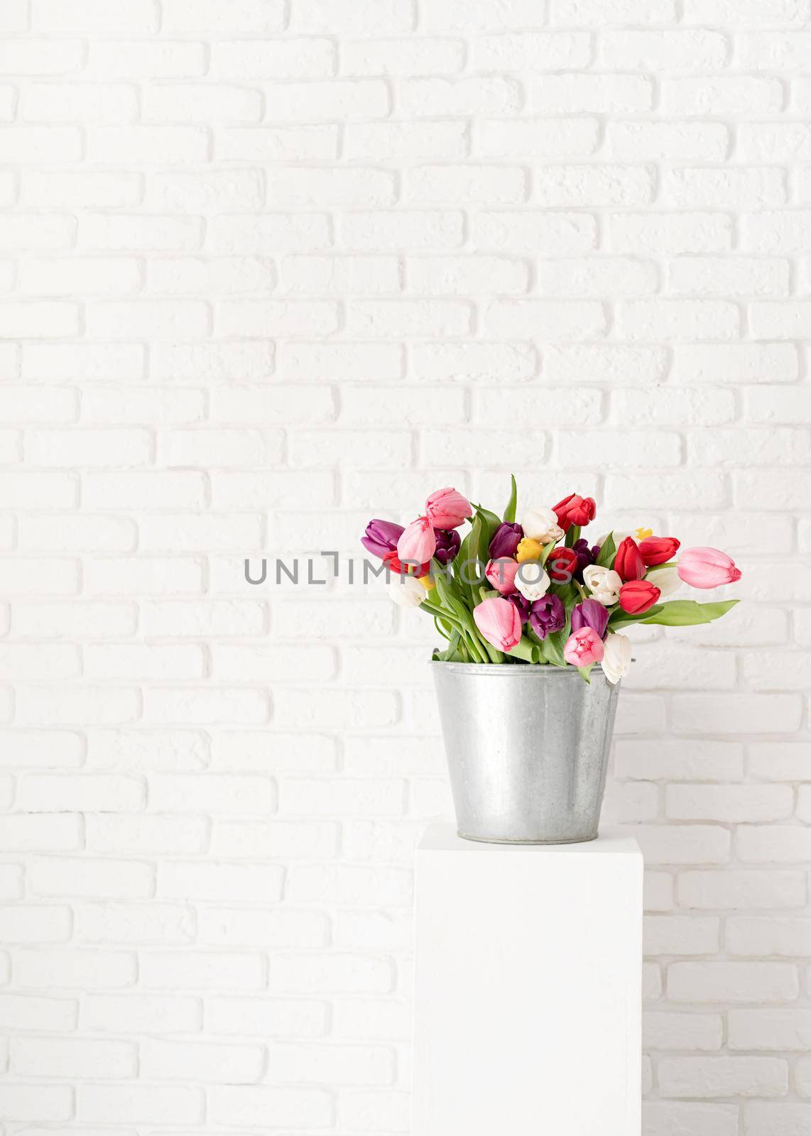 Bucket of tulip flowers over white brick wall background by Desperada