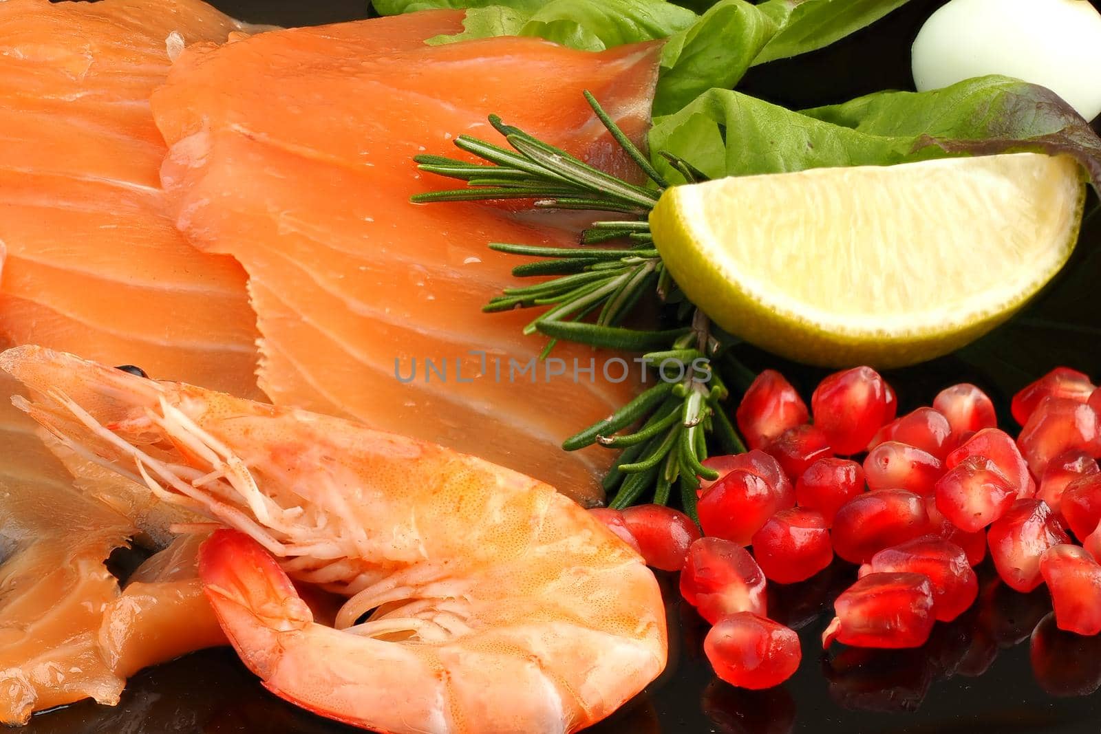 Appetizing slices of sliced salmon with lemon shrimp and pomegranate on a black plate, delicious food. High quality photo