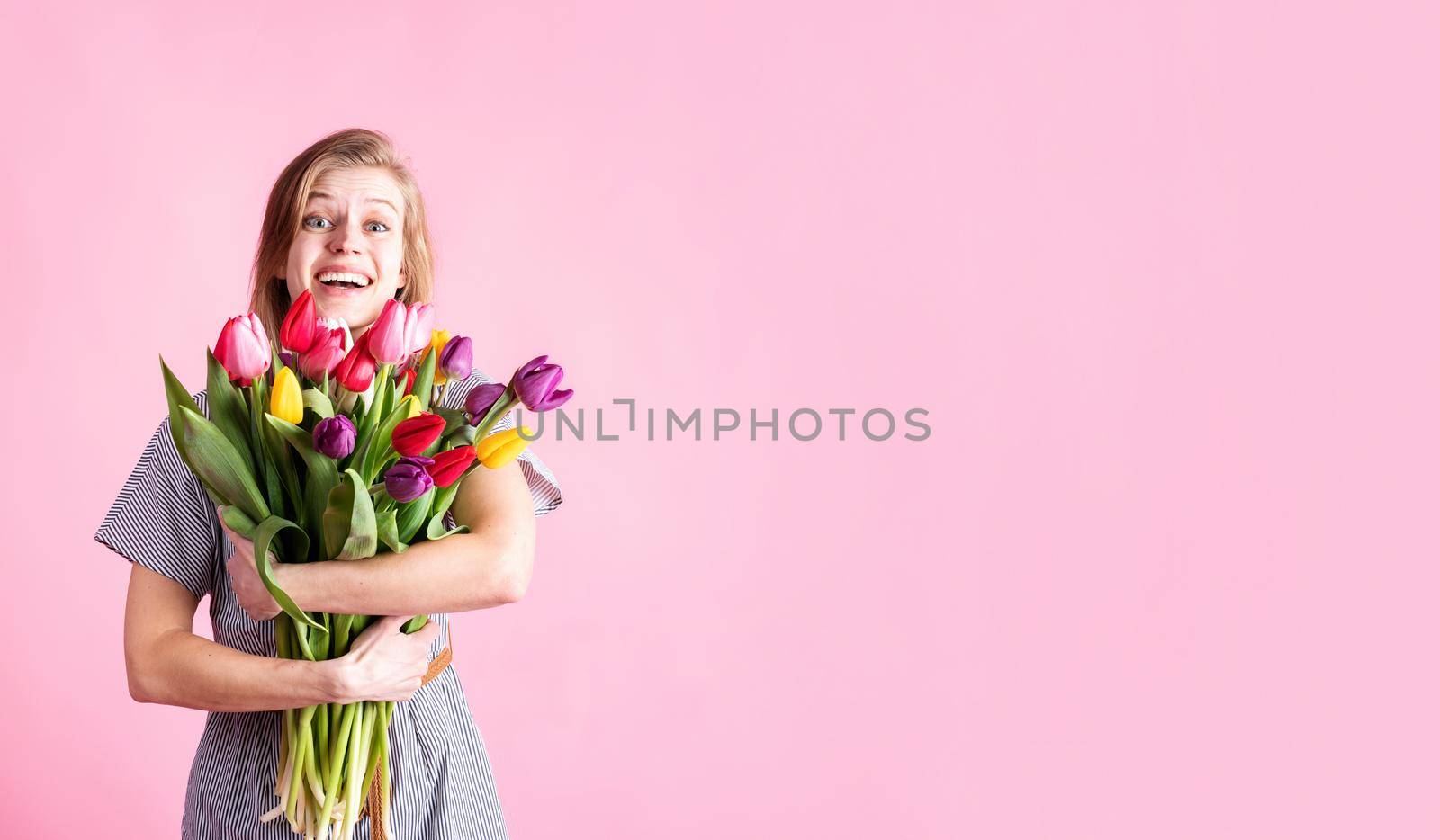Happy young woman holding bouquet of fresh tulips isolated on pink background by Desperada