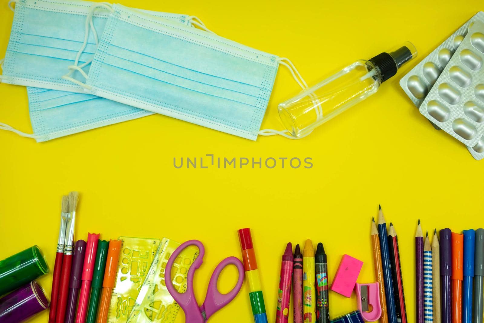 School supplies like pencil scissor eraser ruler watercolor mask alcohol sanitizer on yellow background. Back to school concept during covid pandemic with copy space