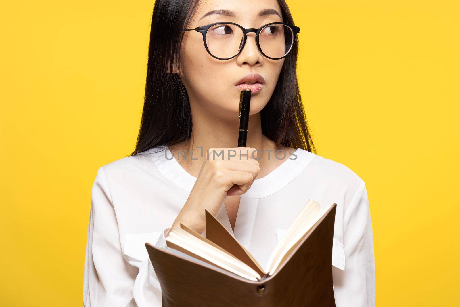 Business woman with a notebook in her hands holds a pen near her lips elegant style yellow background. High quality photo