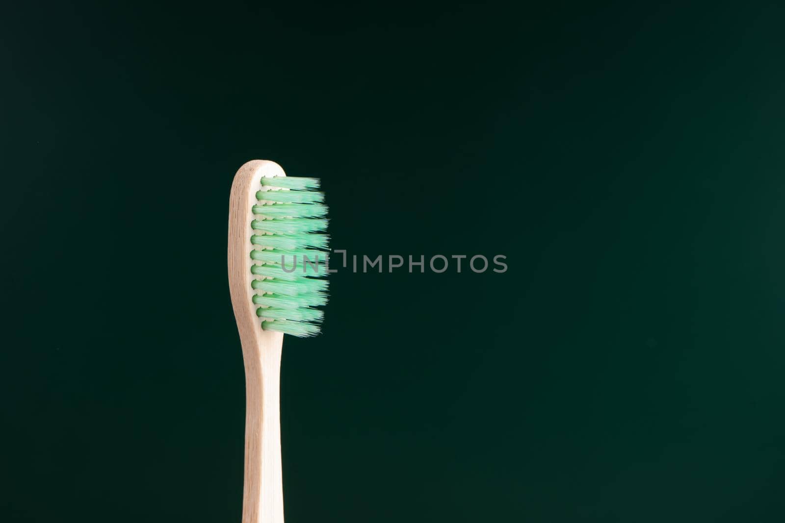 Eco-friendly antibacterial bamboo wood toothbrush on dark green background. Taking care of the environment in trend by Try_my_best