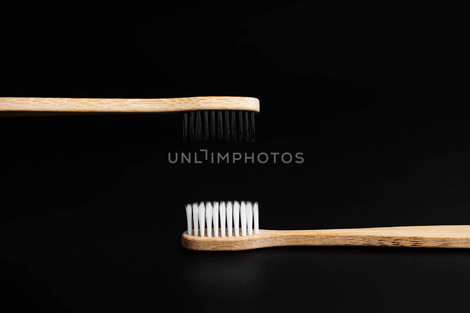 Two Eco-friendly antibacterial bamboo wood toothbrushes with white and black bristles on a black background. Taking care of the environment is trending. Tolerance. Copy space by Try_my_best