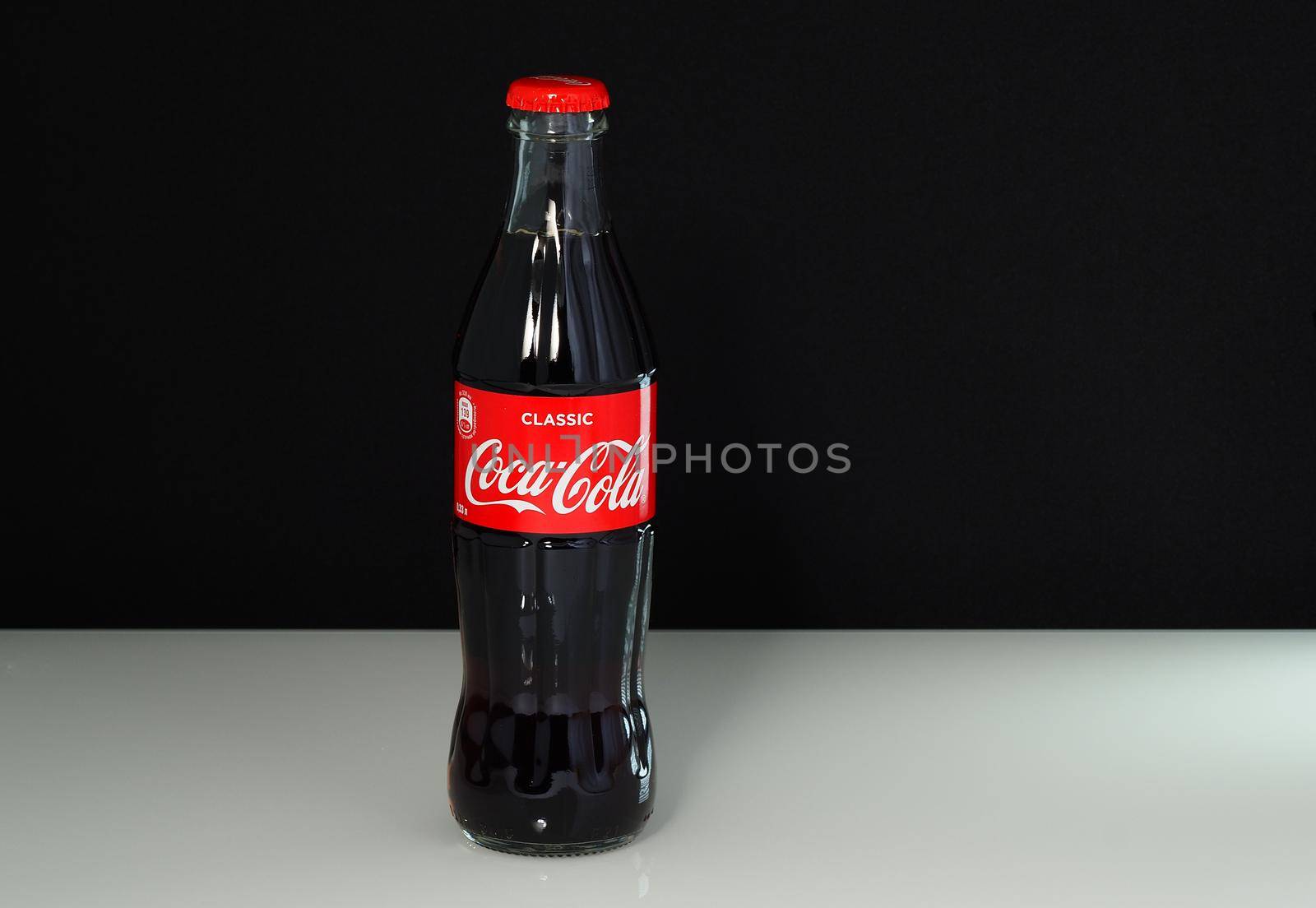 Coca cola, a classic glass bottle with a logo and red lid, is insulated on a black-and-white glass background. High quality . Russia, Nizhny Novgorod, 20.02.2021 