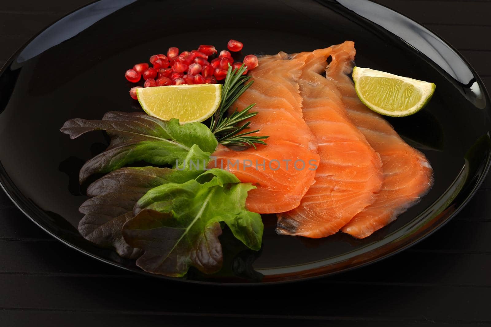 Salmon, sliced red fish with lime, rosemary and pomegranate seeds, served on a black background. Red fish . by Olga26