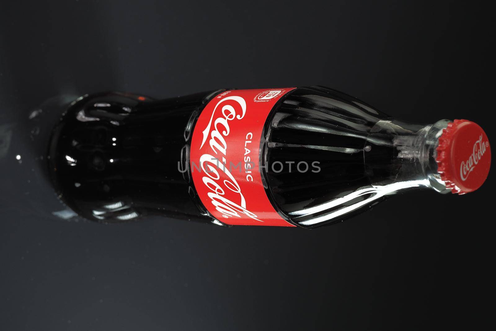 Coca cola. A classic glass bottle of Coke with a red lid and reflection on a glass surface, insulated on a black background. High quality photo