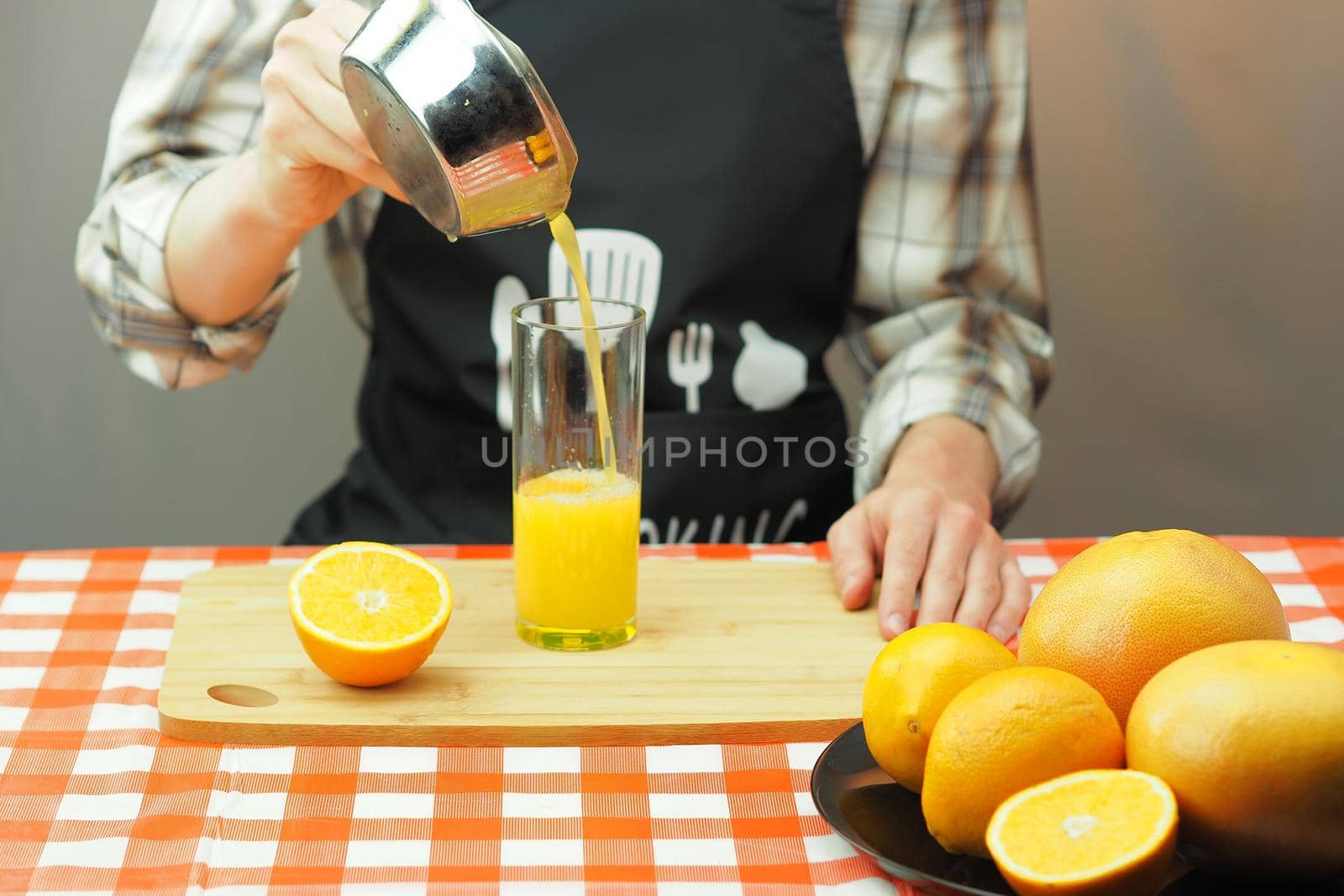 A young man pours freshly squeezed citrus juice into a transparent glass. High quality photo