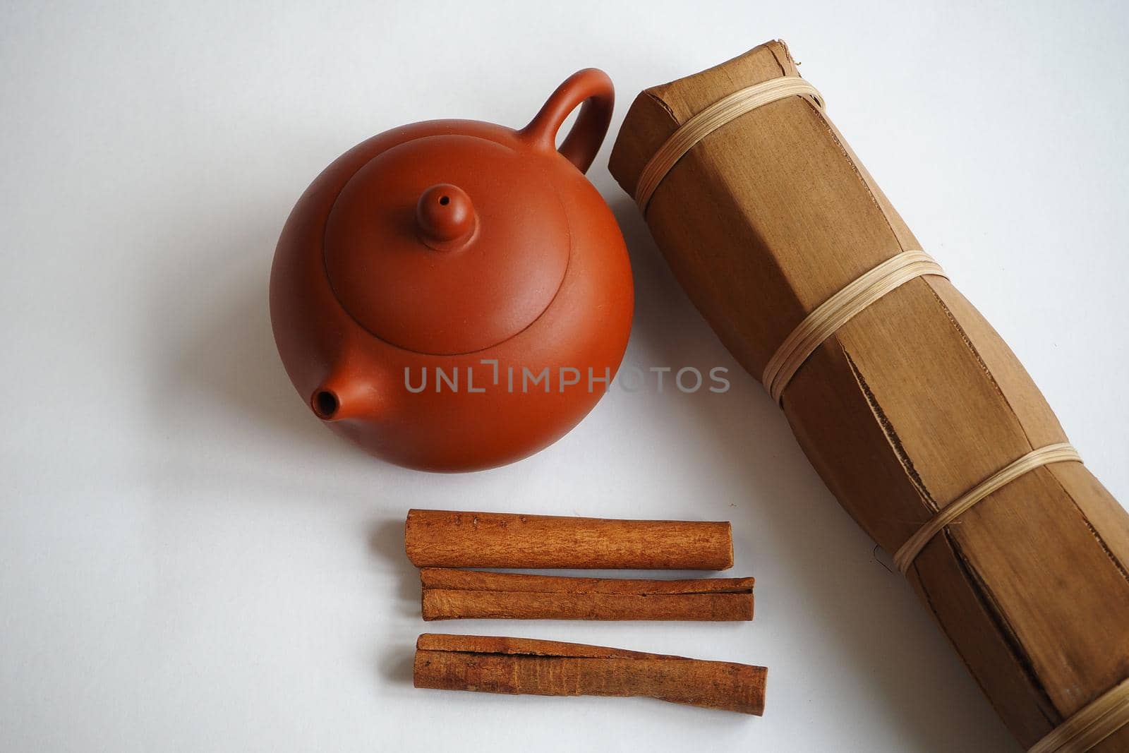 Chinese clay teapot for a tea ceremony with cinnamon sticks and dried herbs on a white background.