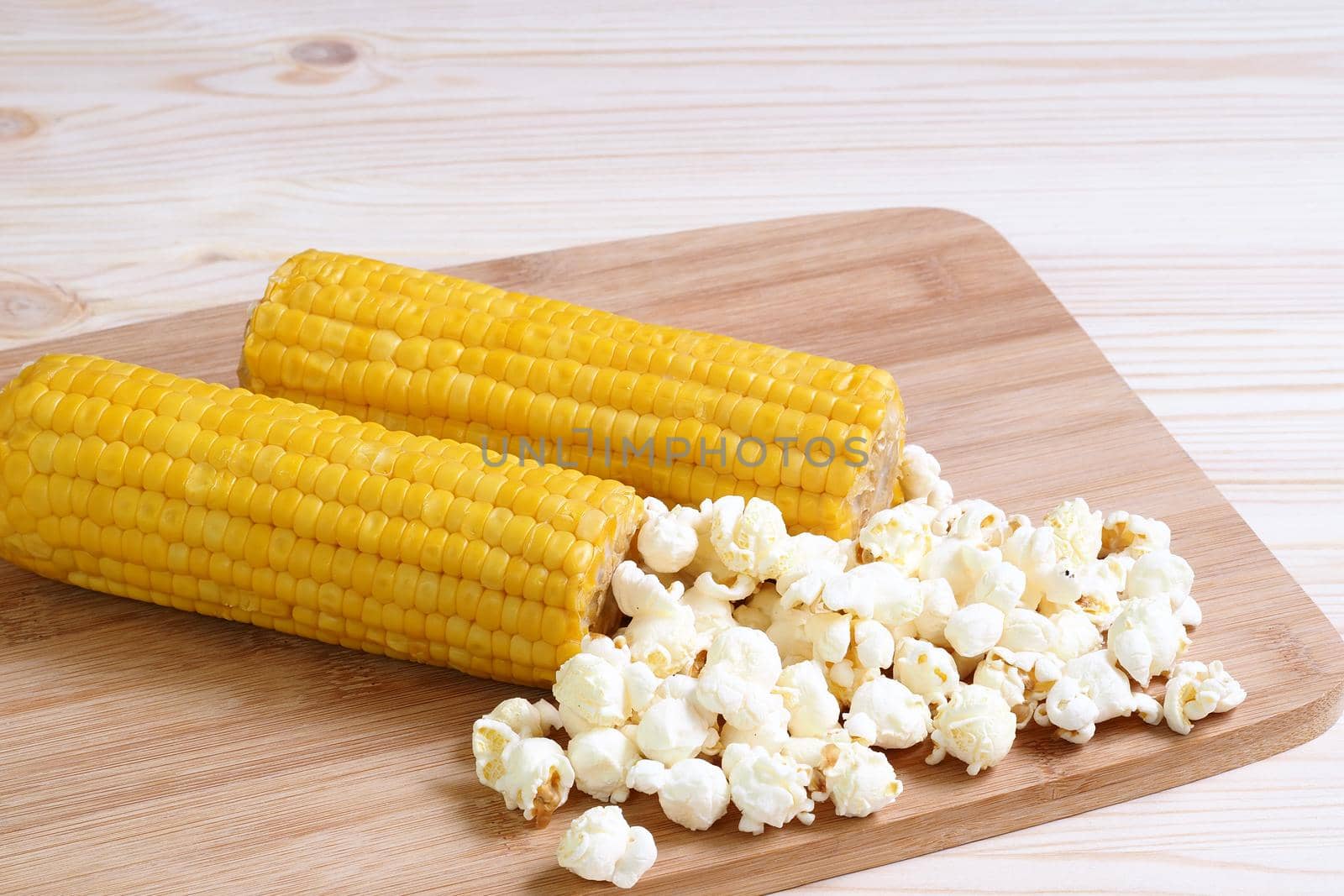 Boiled corn pob and sweet popcorn. Ears of cooked sweet corn on a wooden table scattered popcorn. High quality photoBoiled corn pob and sweet popcorn. Ears of cooked sweet corn on a wooden table scattered popcorn. Close-up, isolated.