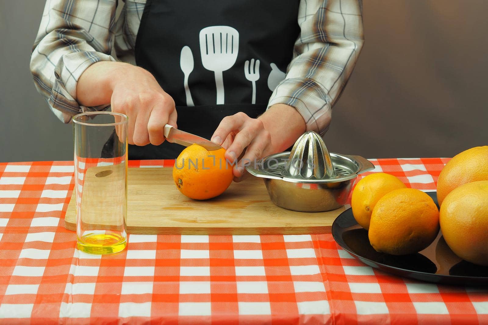 A young man in an apron makes freshly squeezed juice from orange and grapefruit. by Olga26