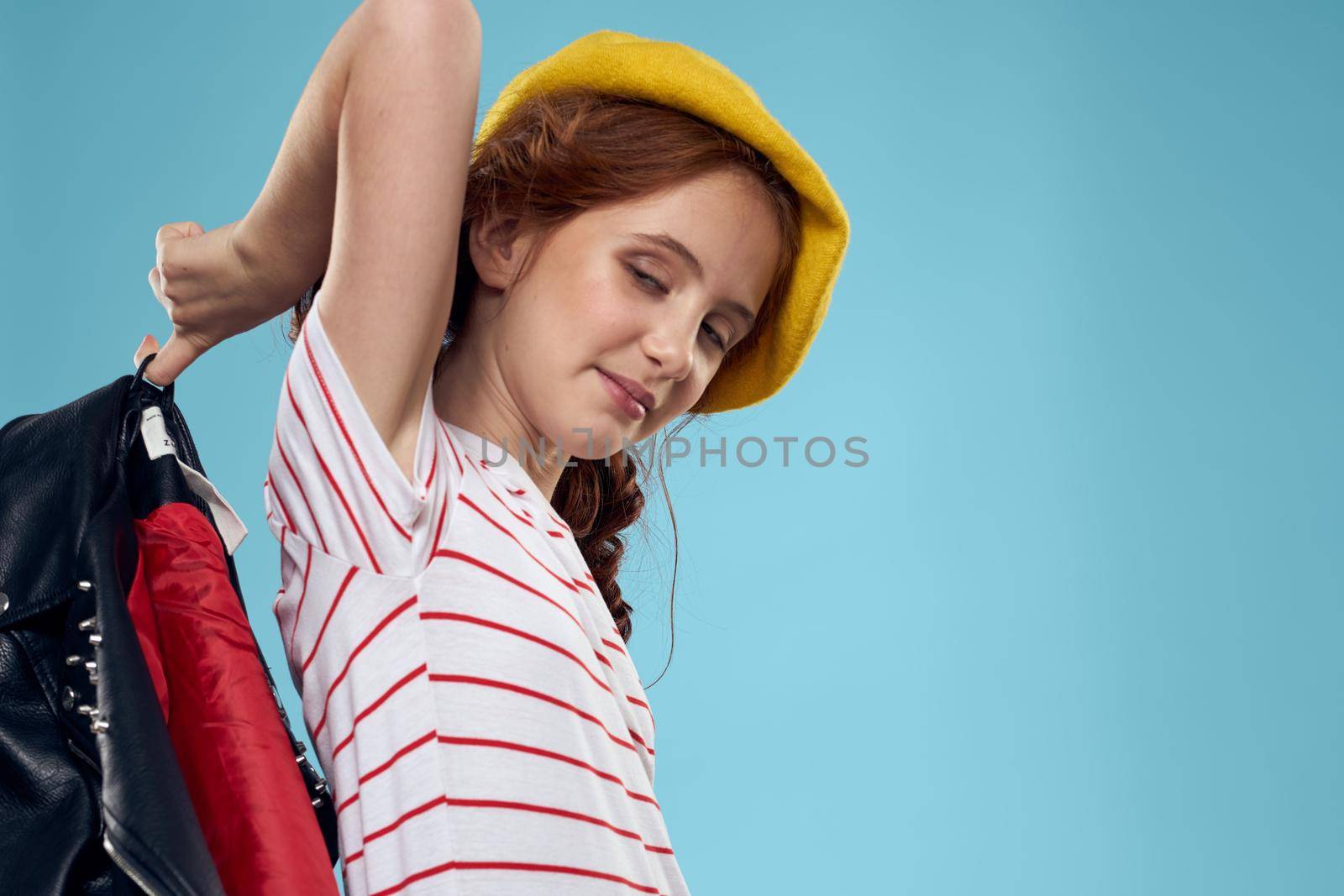 Fashionable girl in a black leather jacket on a blue background and a yellow hat on her head. High quality photo