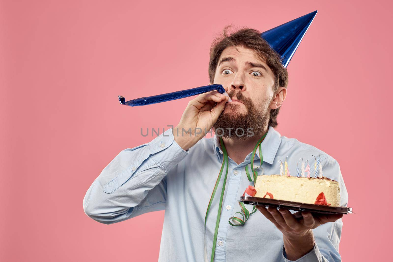 Bearded man with cake tongue on a pink background cropped view and a blue cap on his head. High quality photo