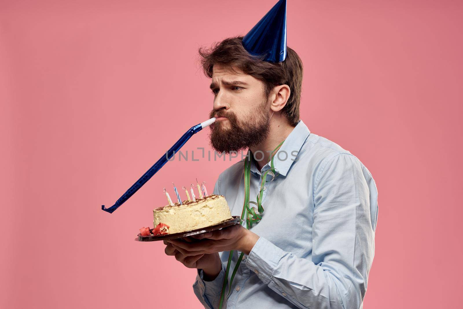 Bearded man with cake tongue on a pink background cropped view and a blue cap on his head. High quality photo