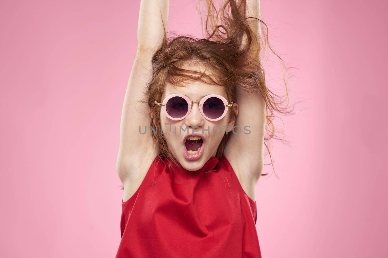 Cheerful little girl childhood dark glasses red dress lifestyle pink background. High quality photo