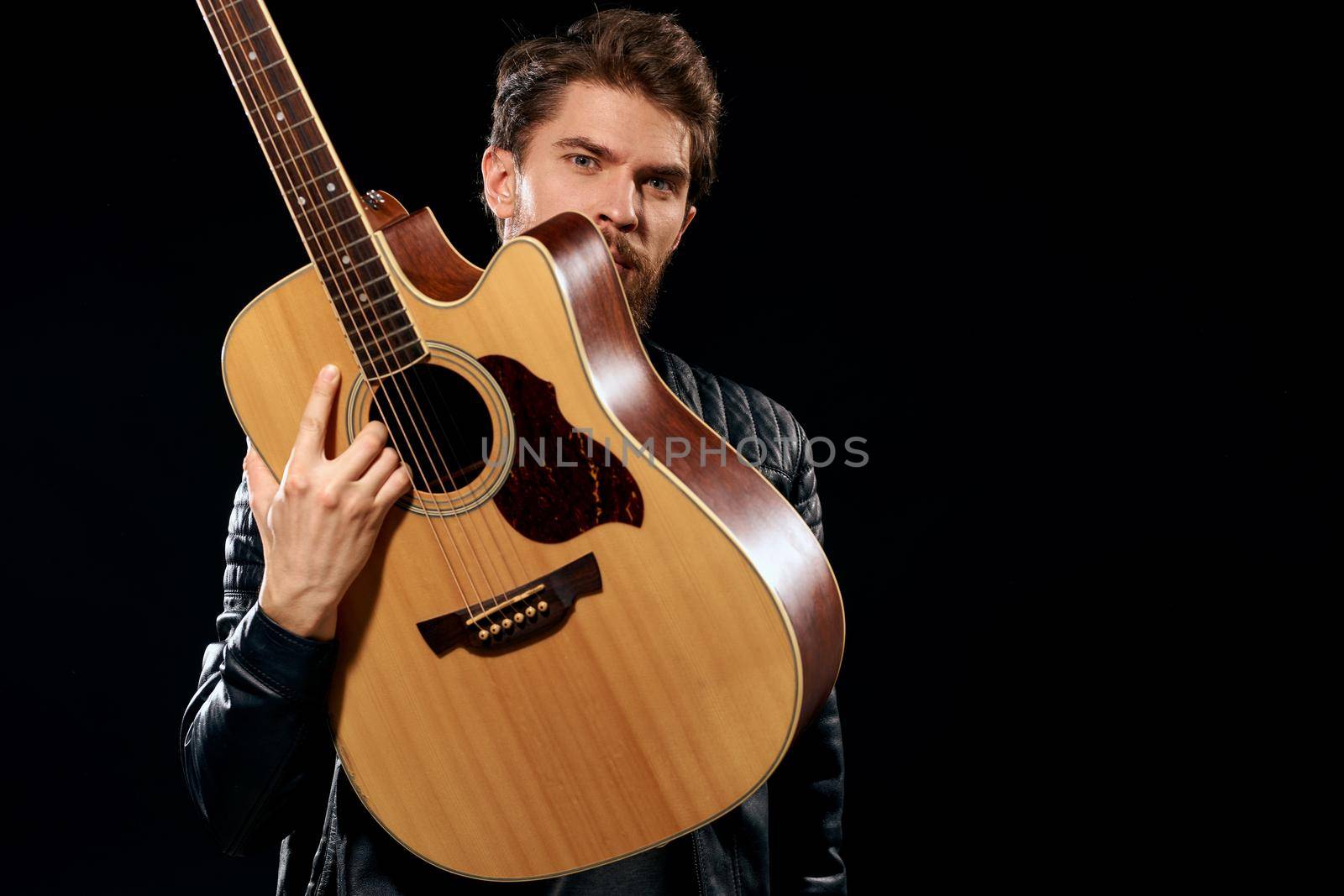 A man with a guitar in his hands leather jacket music performance rock star modern style dark background. High quality photo