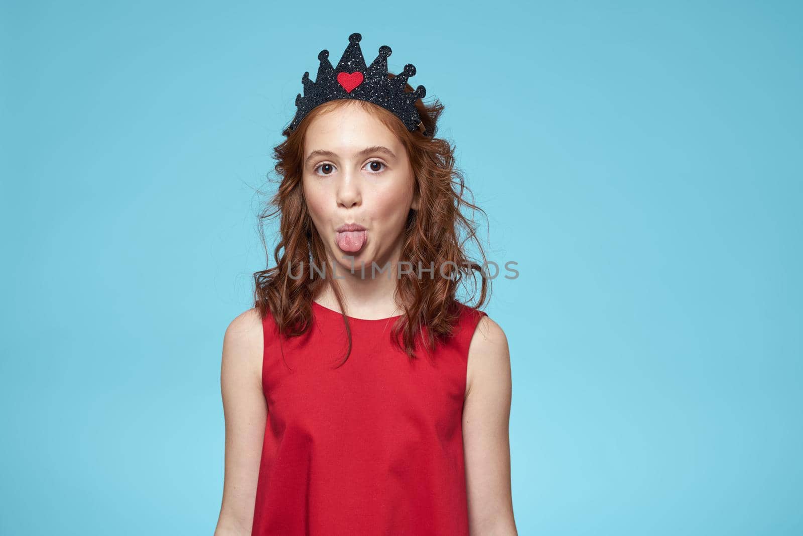 Girl with curly hair with a crown on her head red dress lifestyle blue background. High quality photo