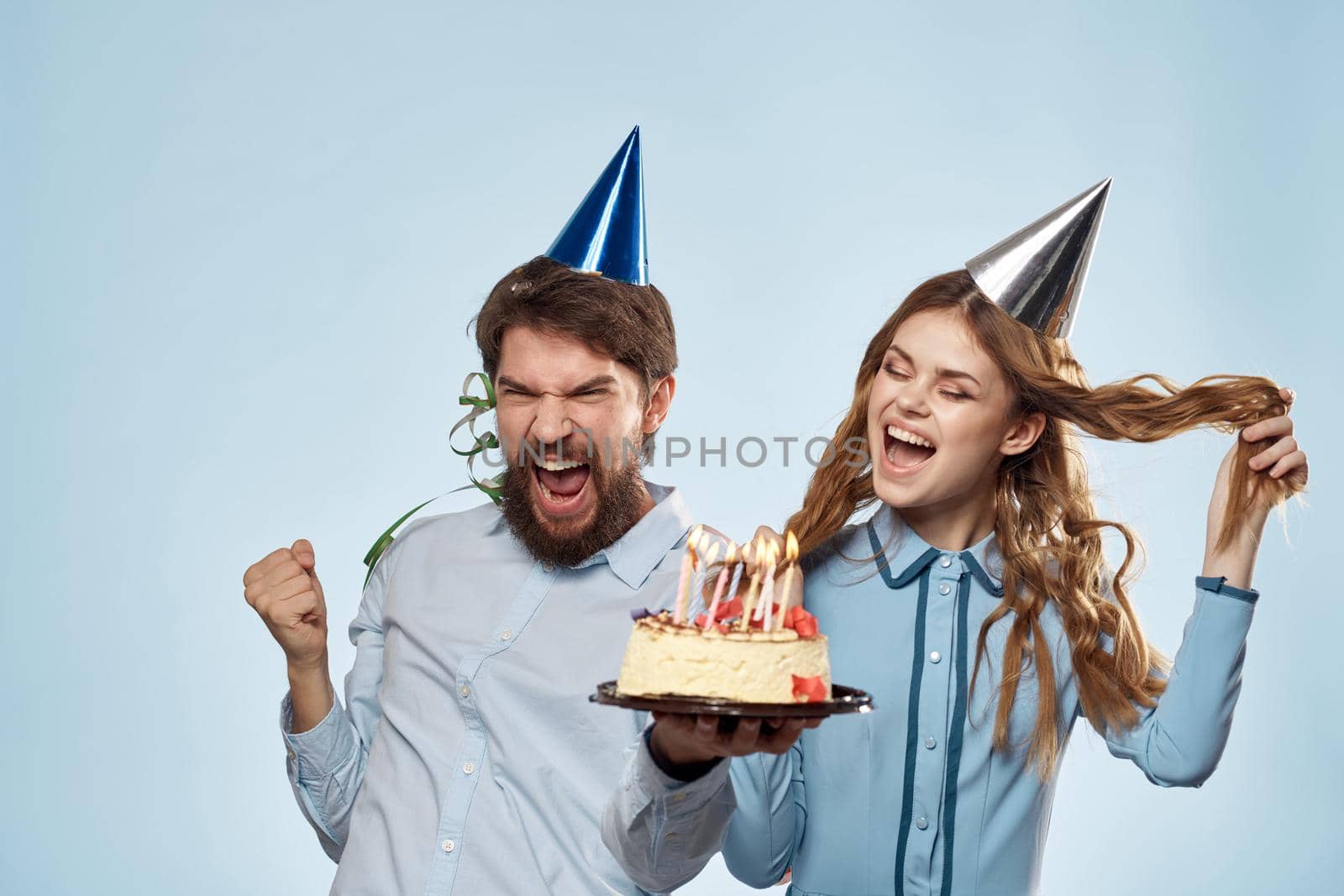 man and woman celebrate birthday with cake and in hats on blue background. High quality photo