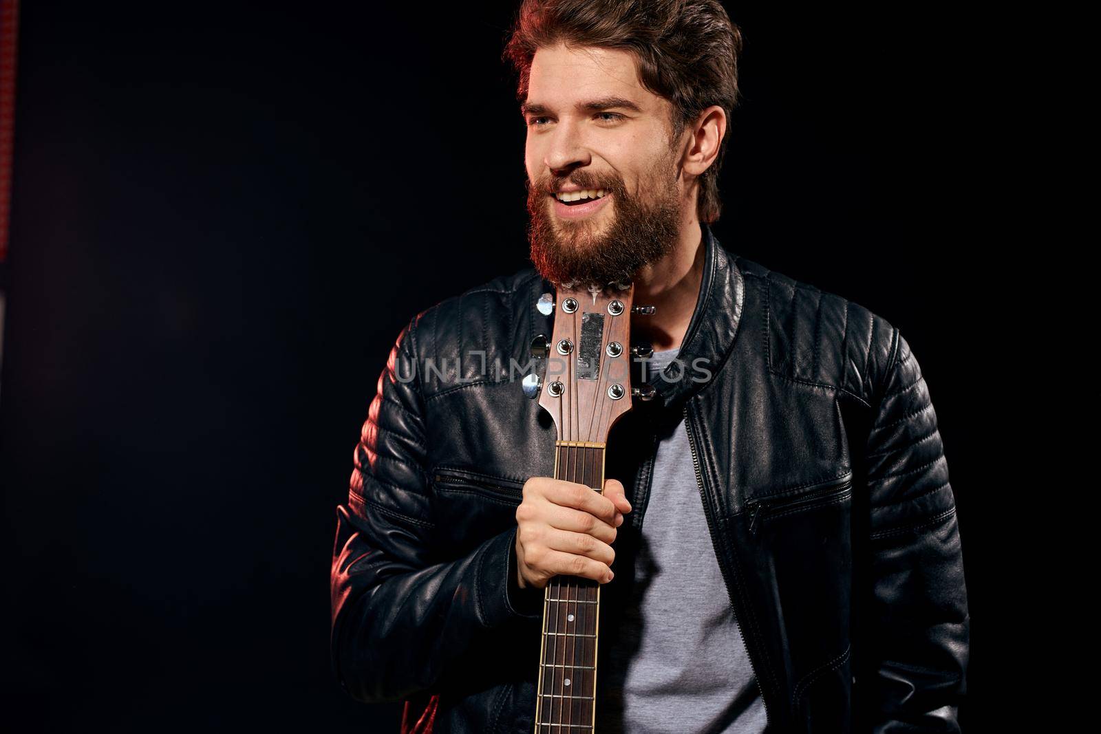 A man with a guitar in his hands leather jacket music performance rock star modern style dark background. High quality photo