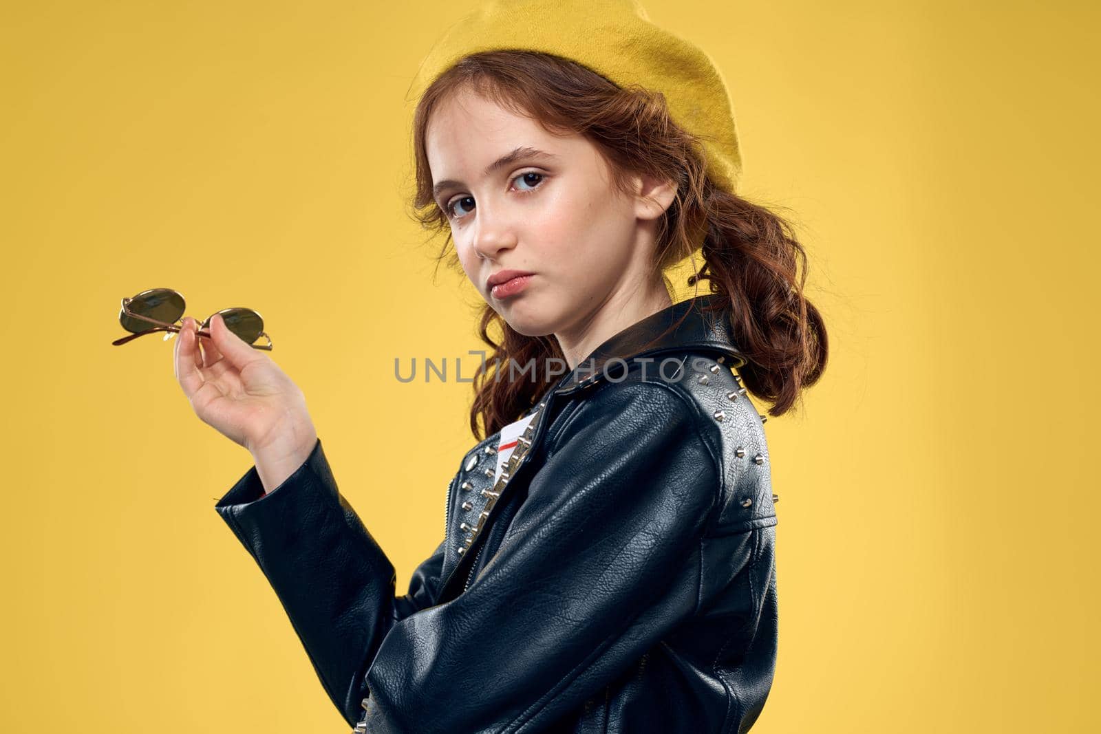 Cheerful little girl in sunglasses and hat lifestyle studio yellow background fashion. High quality photo