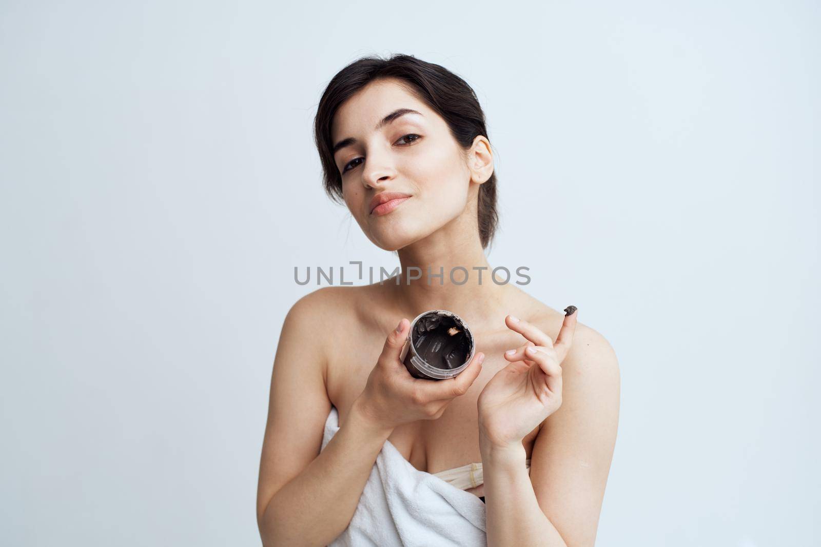 Pretty woman in white towel naked shoulders black cream in hands skin care spa procedure. High quality photo