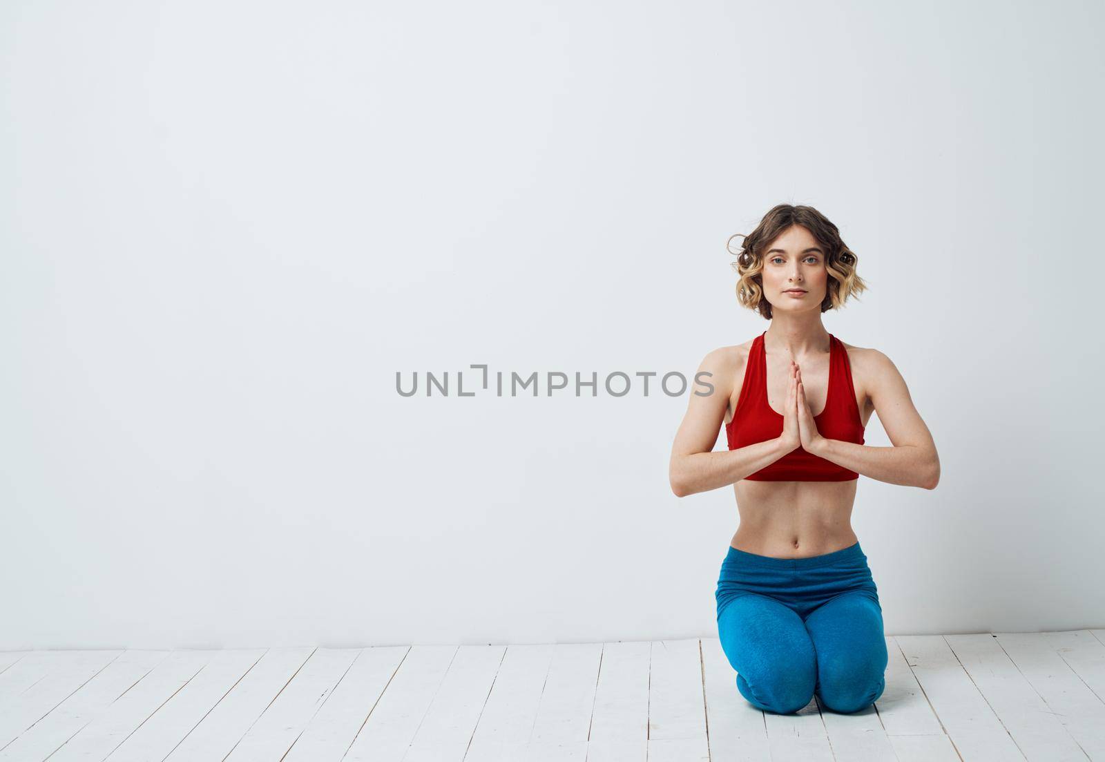 A woman sits on a light floor indoors with her hands joining yoga asanas for relaxation by SHOTPRIME