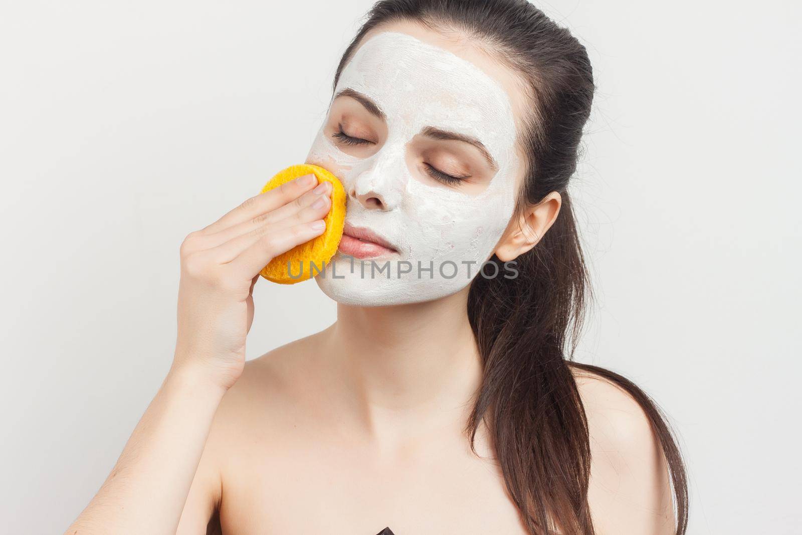 Cheerful brunette wipes her mask with a sponge scrub skincare. High quality photo