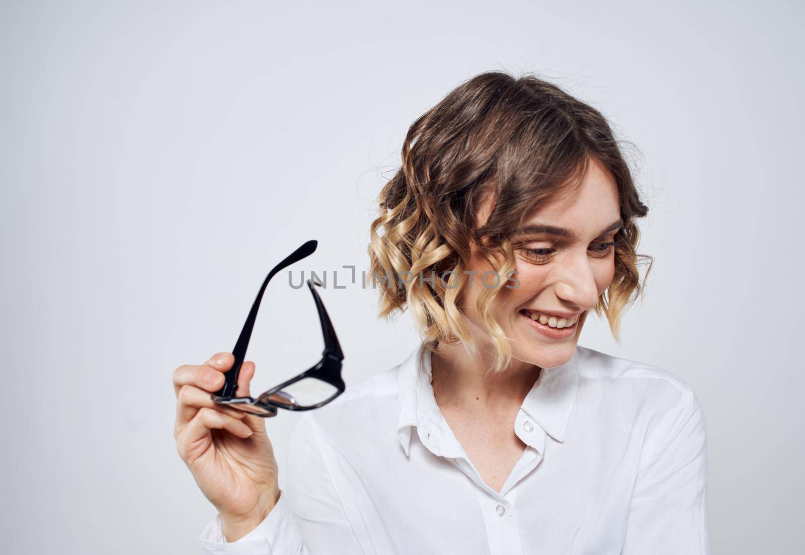 A woman with a short haircut and a white shirt holds glasses in her hands. High quality photo