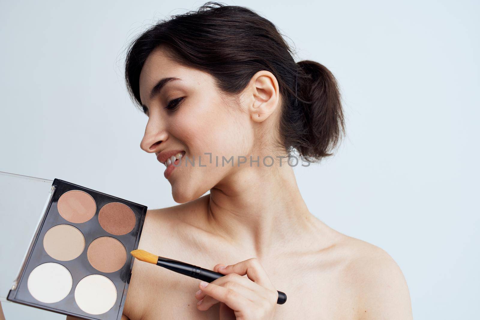 Pretty woman with naked shoulders applying makeup on face lifestyle. High quality photo