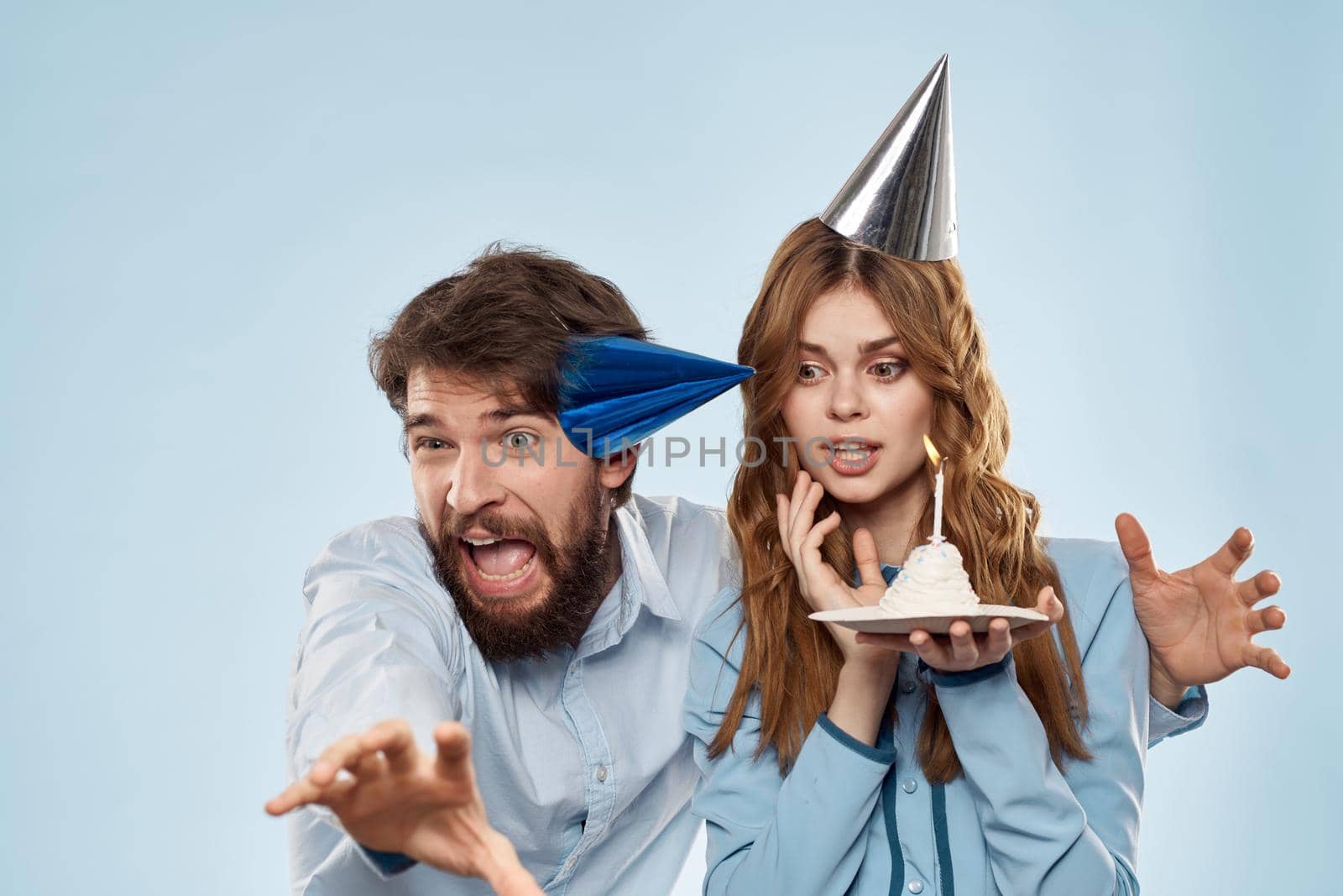 Cheerful man and woman blowing out cake candles holiday decoration blue background by SHOTPRIME