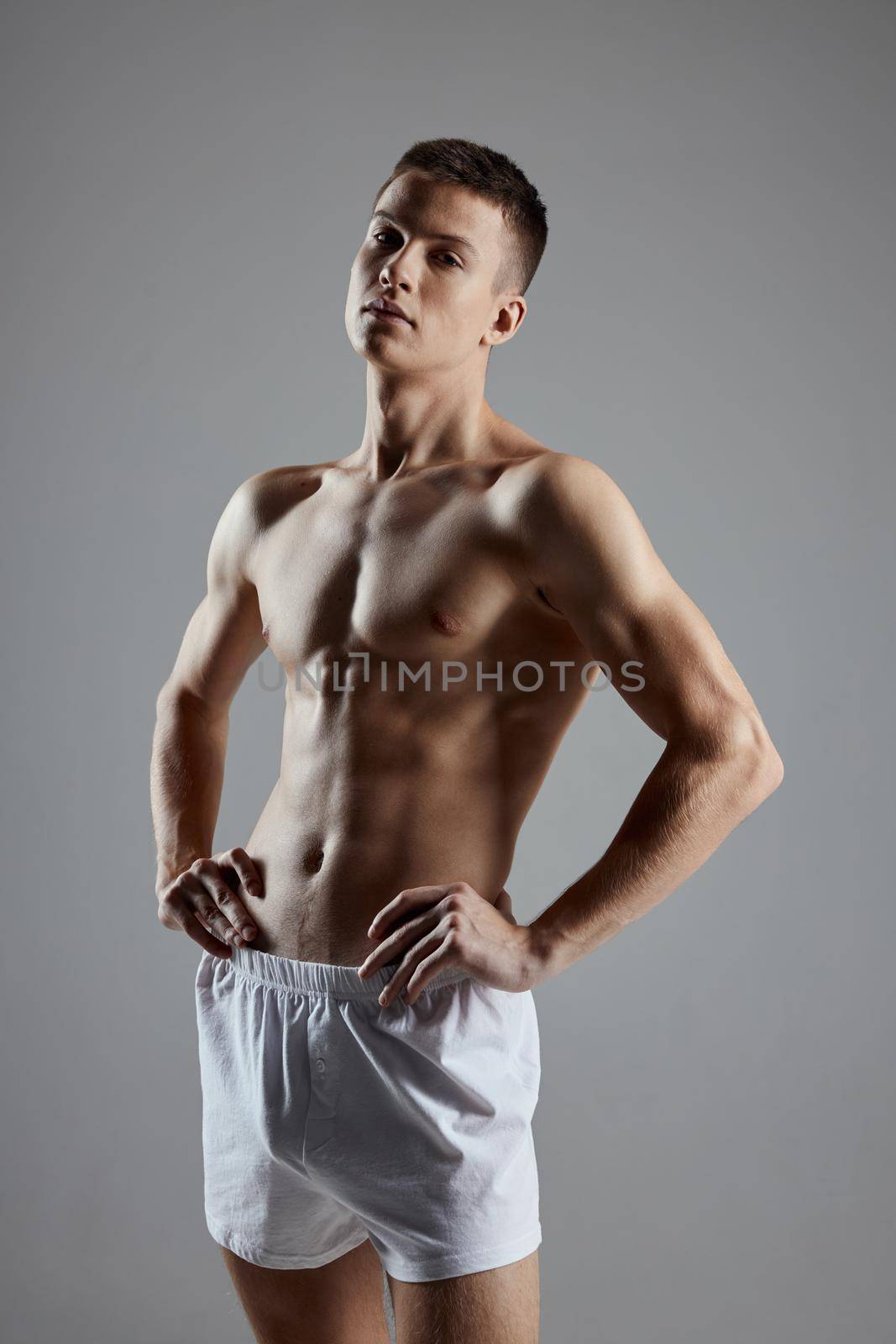 a guy with an athletic physique in shorts holds his hands on the belt on a gray background. High quality photo