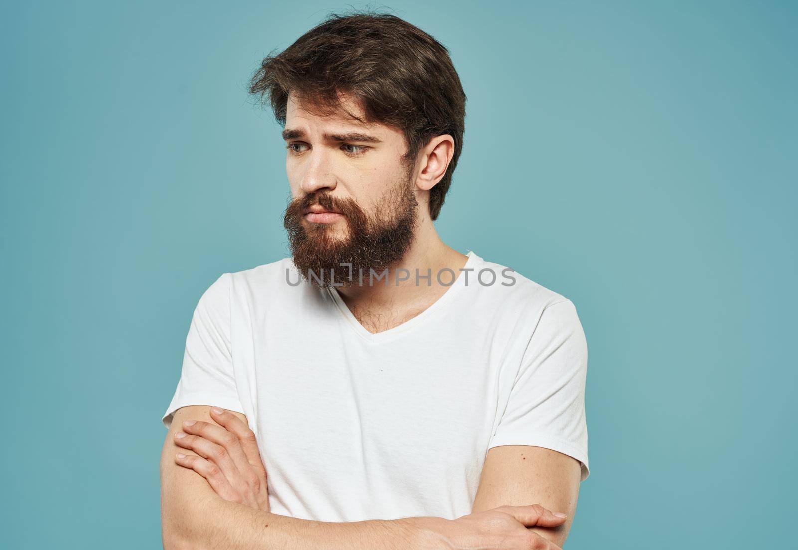a man in a white t-shirt on a blue background gestures with his hands sad look. High quality photo