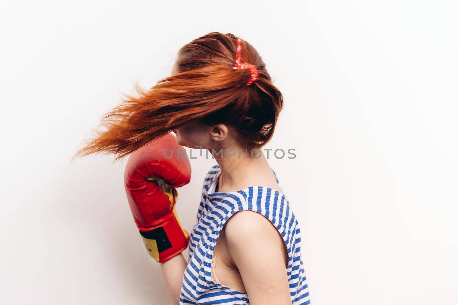 woman practicing a blow in boxing gloves on a light background striped t-shirt model. High quality photo