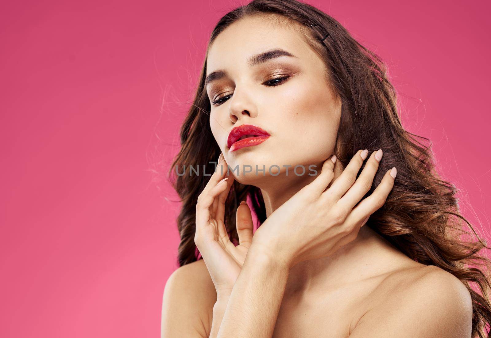 Sexy brunette with red lips on a pink background touch her hair with her hands. High quality photo