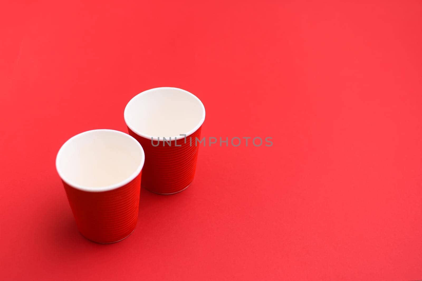 Two empty red paper cups. On a red background. Disposable eco-friendly glasses. copy space