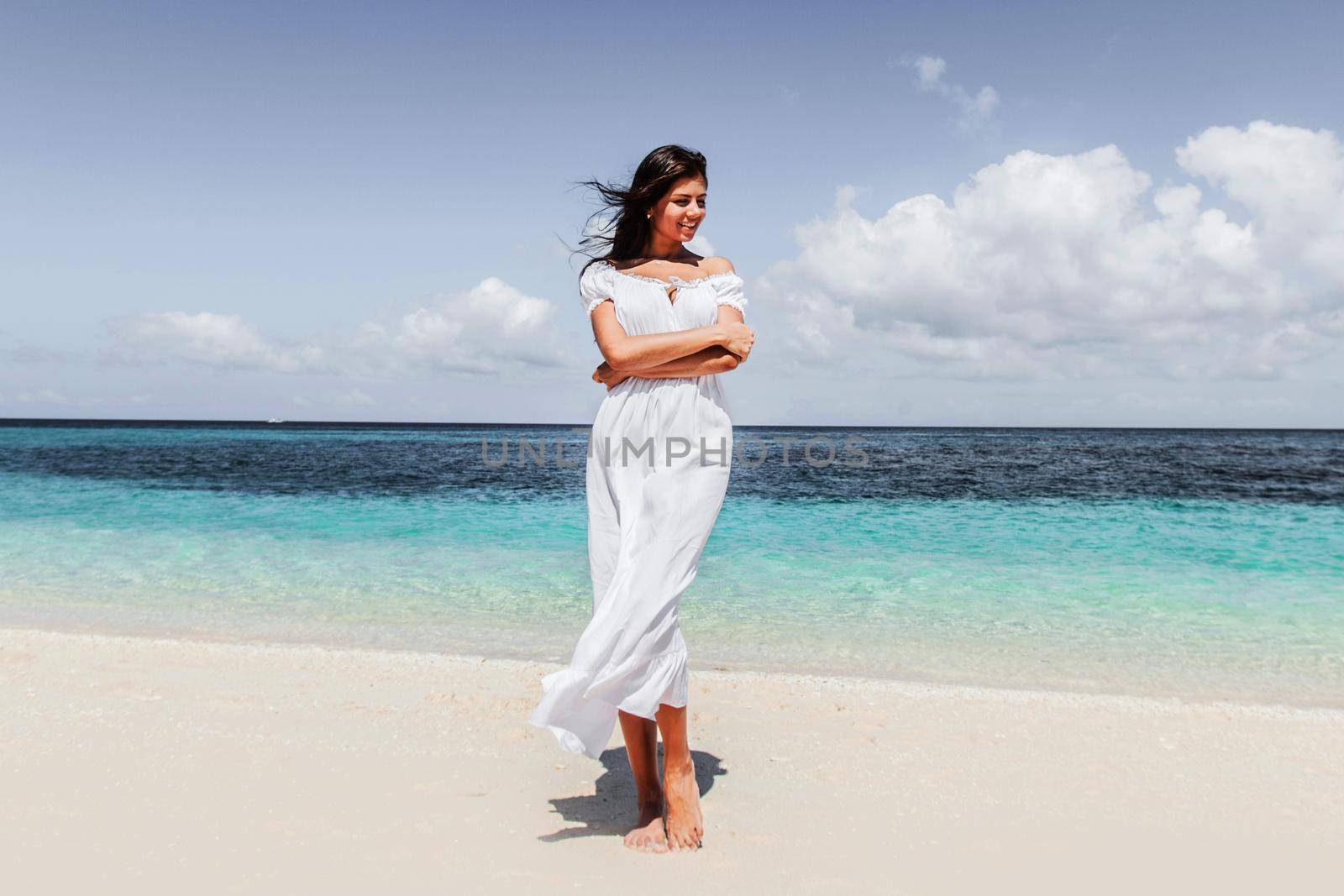 Woman in white dress walking on tropical beach, tropical sea on background