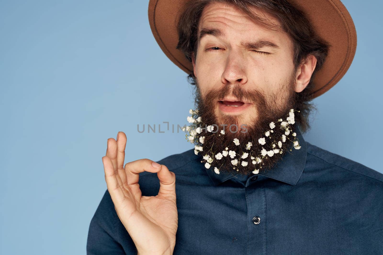 Cute man in a hat flowers in a beard emotions close-up blue background. High quality photo