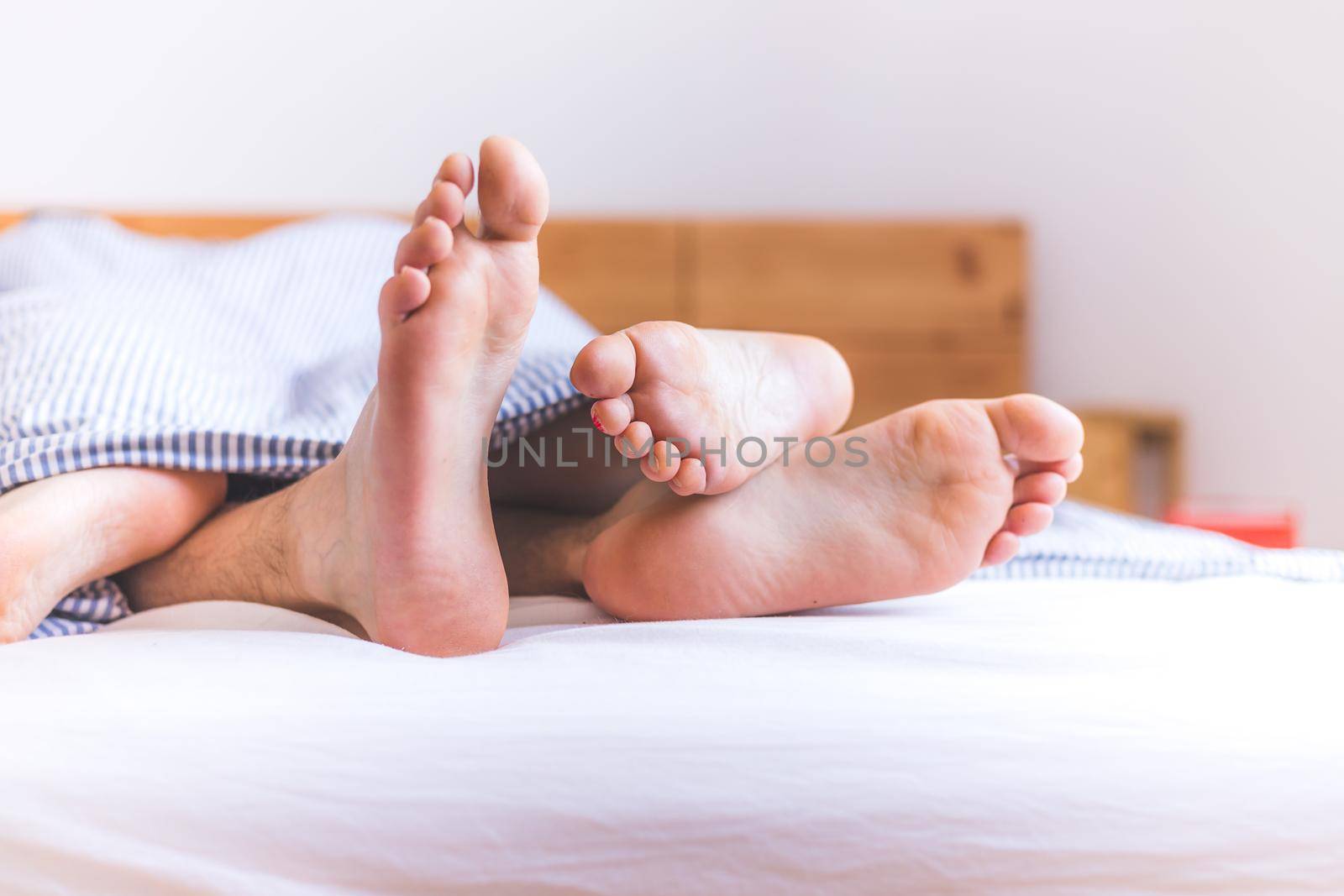 Close up a couples uncovered feet sleeping in bed, morning