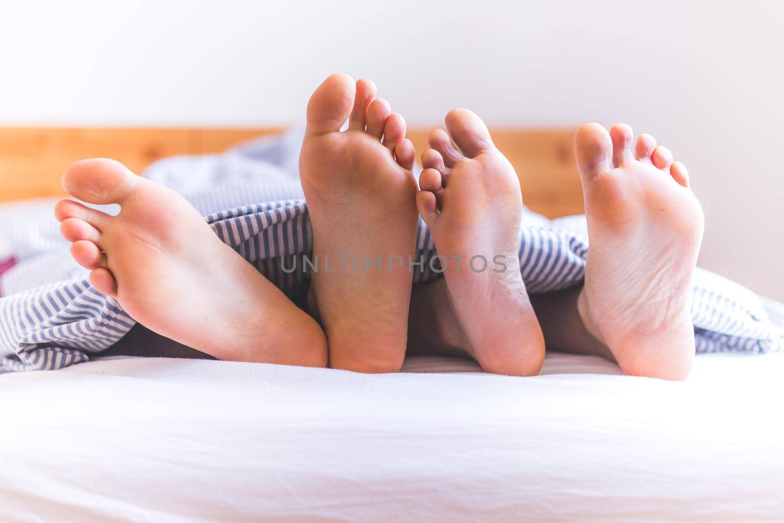 Close up a couples uncovered feet sleeping in bed, morning