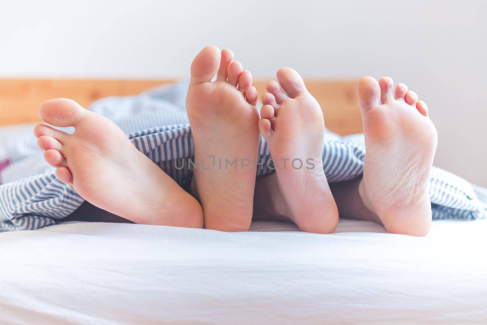 Close up a couples uncovered feet sleeping in bed, morning