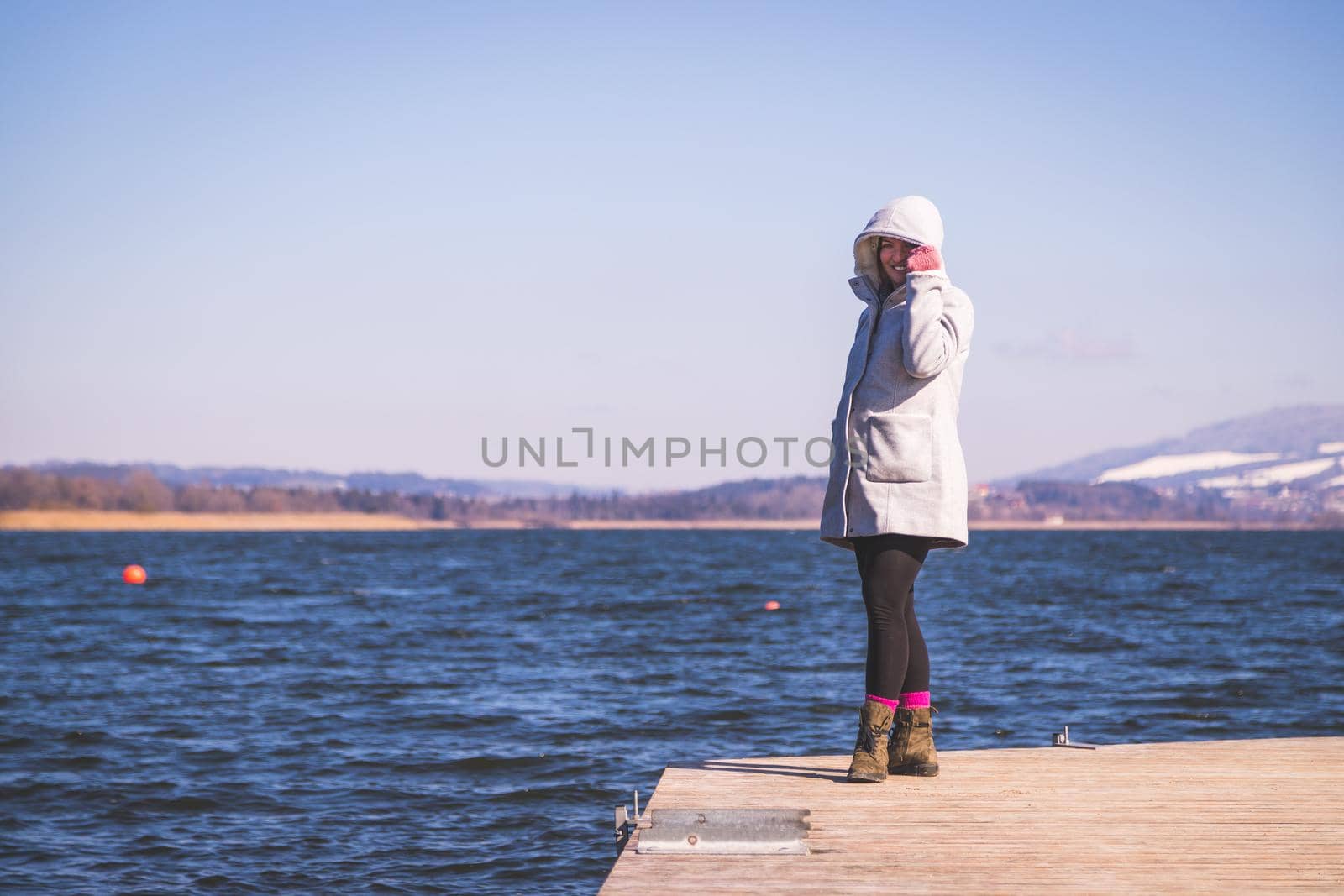 Beautiful young woman with grey coat is standing on a footbridge and enjoying the view, winter time by Daxenbichler