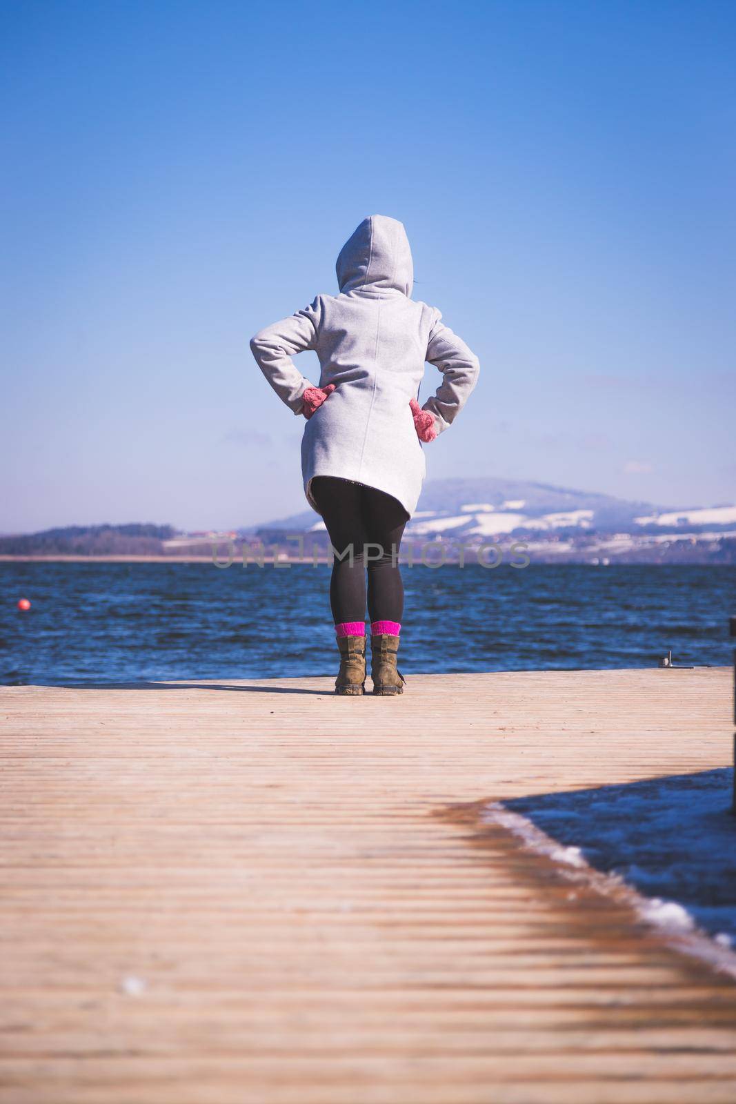 Beautiful young woman with grey coat is standing on a footbridge and enjoying the view, winter time by Daxenbichler